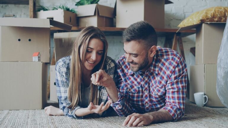 Couple lying on the floor among moving boxes while holding house keys during a

home transition.
