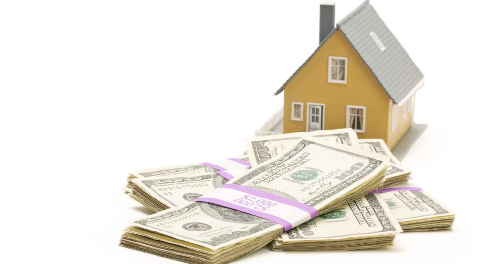 Cash and small house model on table symbolizing fast cash home buying in real estate.