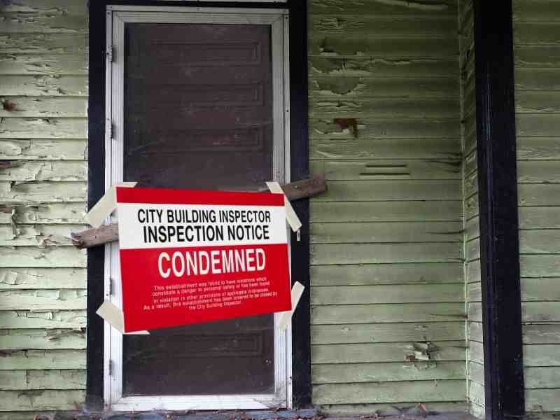 Exterior of a condemned house with a "condemned" sign on the door.
