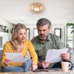 Middle-aged couple evaluating a cash offer on their home amidst paperwork and a calculator.