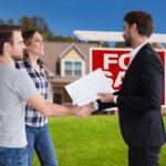 Young couple and real estate agent handshaking in front of a sold Sacramento house at sunset.