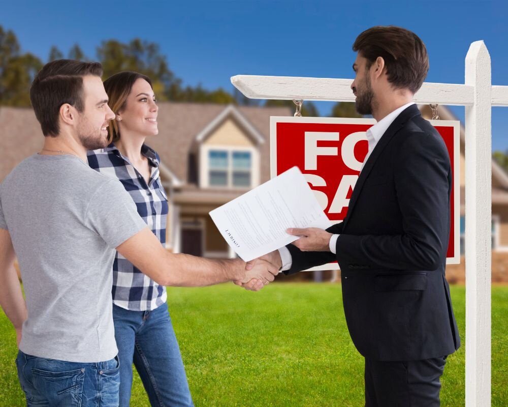 Young couple and real estate agent handshaking in front of a sold Sacramento house at sunset.