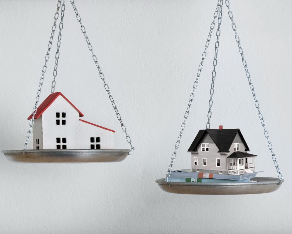Two house models on a balance scale, comparing cash offer to home value