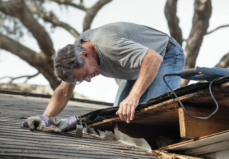 Close up view of man removing rotten wood from leaky roof