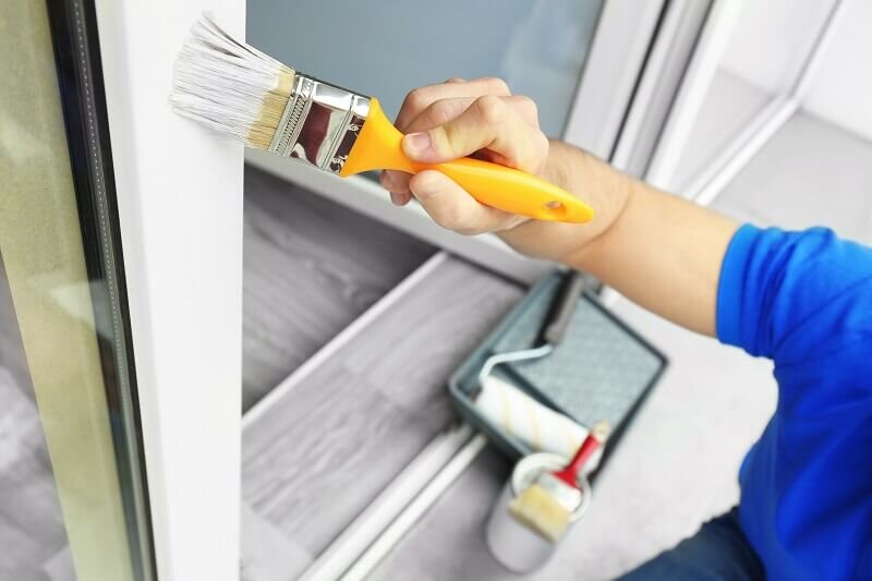 A homeowner painting the frames of his home's windows. Repainting is one of the most common ways to improve the value of your home