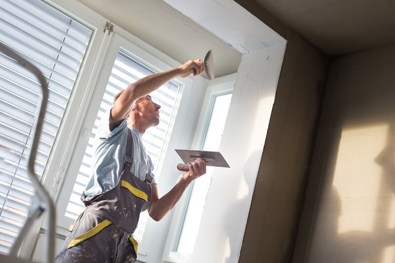 A young worker plastering the walls of a fire damaged house ahead of a repainting job. Repainting is essential if you're trying to repair fire damage.