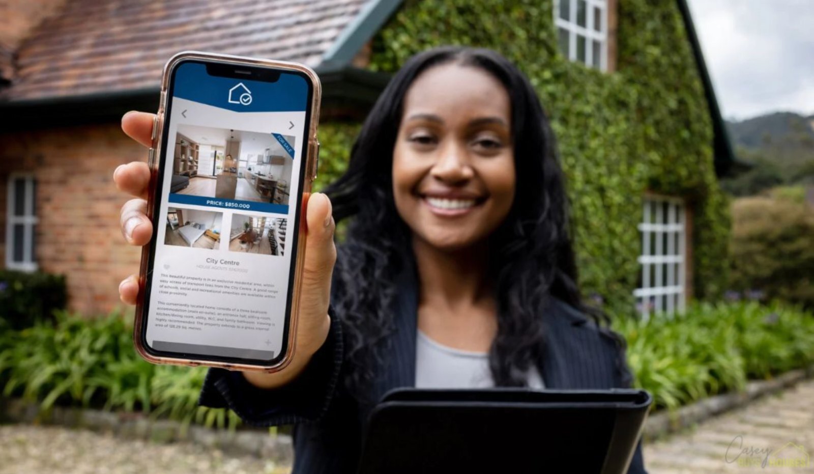 Agent showing home listing photos on a phone outside a house for sale