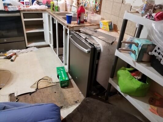 A kitchen in the midst of a rehab project with flooring torn up and part of the counter top removed.