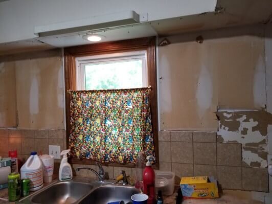 Kitchen sink with counters covered with stuff, before rehab by Anna Buys Houses.