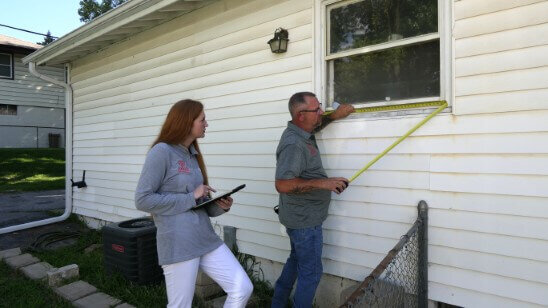 Mark and Mary Craig team members at Anna Buys Houses measure a window on a rehab property.