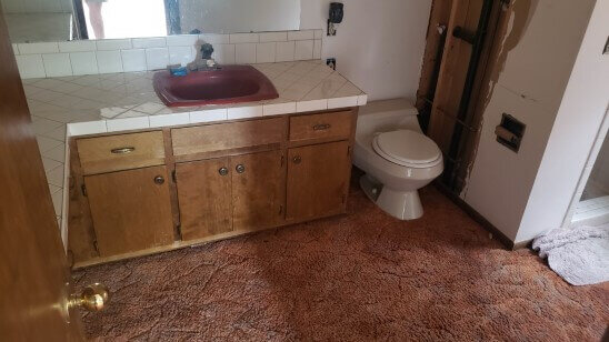 Master bathroom before rehab with carpet and dated sink, tile, and cabinets.