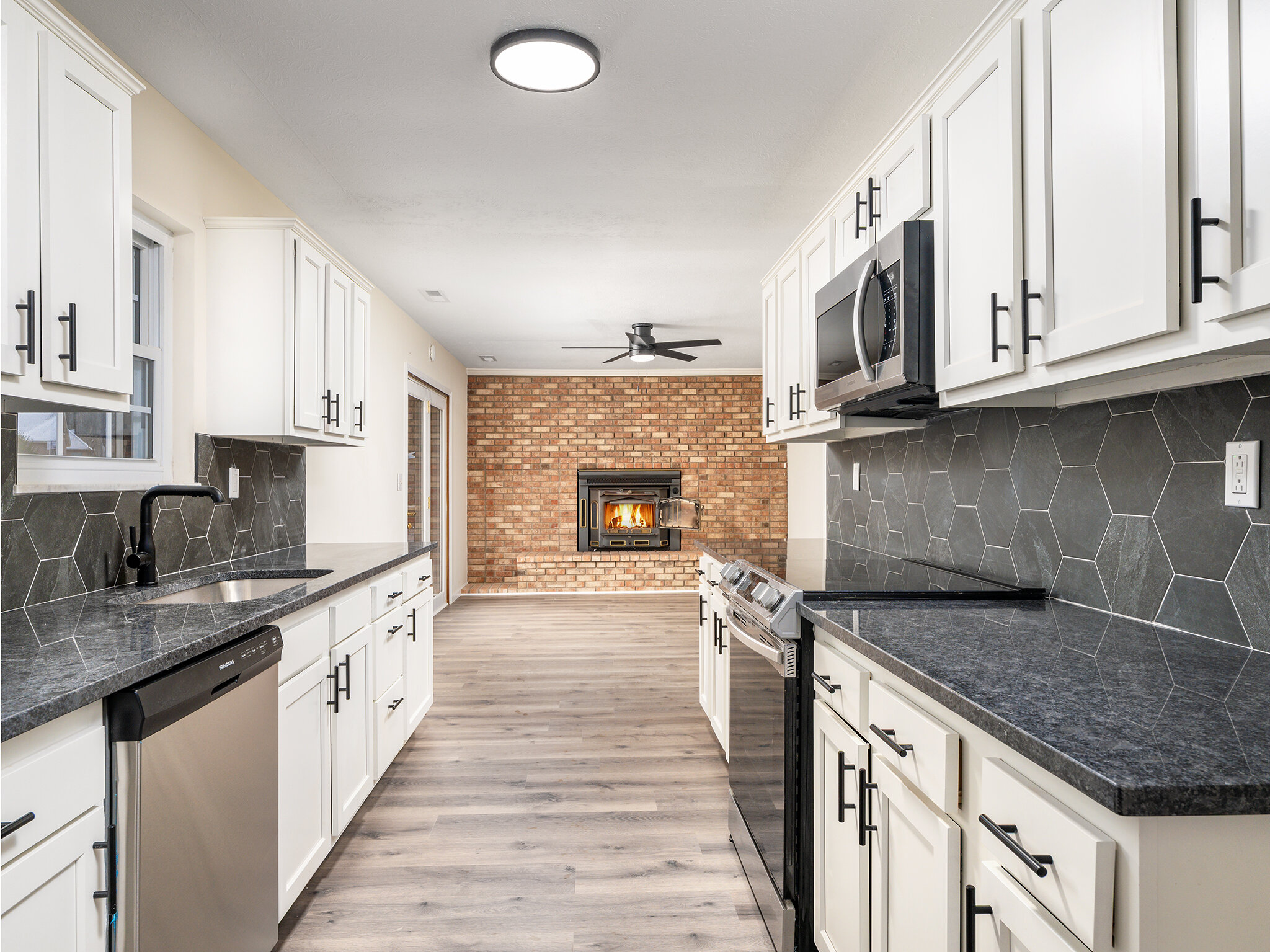 White cabinetry and dark counters in the Woodland Forest kitchen, with an adjoining brick fireplace.