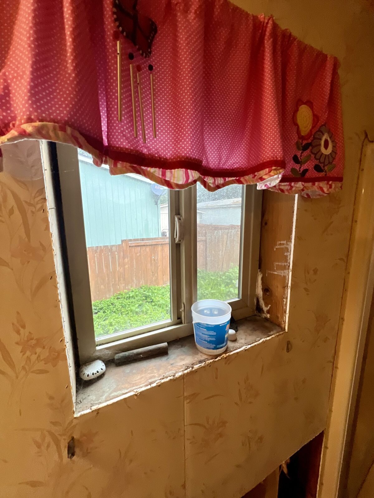 Bathroom window with worn, damaged wall paneling in the Albany manufactured home