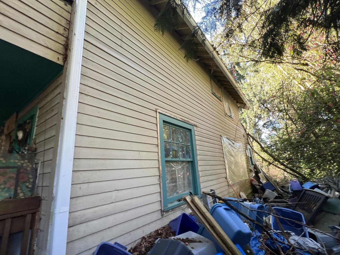 Side wall of the Milwaukie house with blue bins and debris piled along it