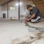 Worker sealing basement floor cracks to protect house from water and to waterproof the basement.