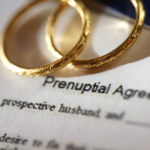 This image captures the essence of pre and postnuptial agreements, highlighting the importance of financial planning in marriage. It features two gold wedding rings resting on a prenuptial agreement document, symbolizing the commitment to securing financial futures and ensuring clarity in marital asset management. Such agreements play a crucial role in outlining the division of assets and protecting individual interests, both before and after tying the knot.