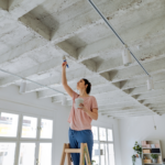 A DIY enthusiast refreshes her living space, painting the ceiling white to brighten up her modern loft.