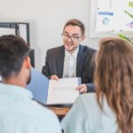 back view of a couple being shown a contract document by a suit. Land Buyers In Alabama - Read These Top Tips Find Them.