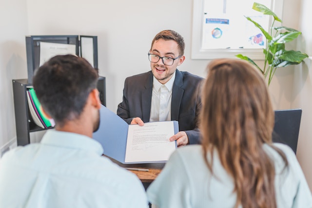 back view of a couple being shown a contract document by a suit. Land Buyers In Alabama - Read These Top Tips Find Them.