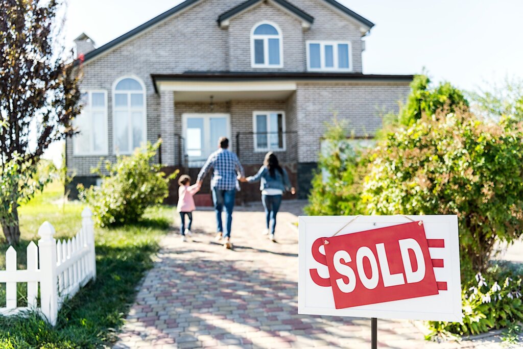 couple and child walking in front of a family house with a sign at the front written in white "Sale" on a red background. 3 Financial Options You Can Pursue When Selling an Inherited Property in Huntsville
