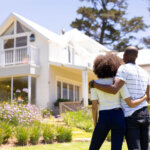 couple standing in front of a house with white exterior walls , white roof and beautiful lawn. Is There A Holding Period Before Selling My Inherited Home? – 35801