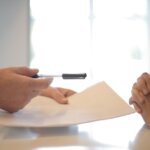 A loan officer handing a pen to the person needing the loan so they can sign the land loan agreement. Understanding How Land Loans Work for Property in Huntsville