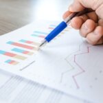 close-up of hand holding a pen on paper with charts on a wooden desk. 4 Things You Should Know About Land Surveys in Huntsville