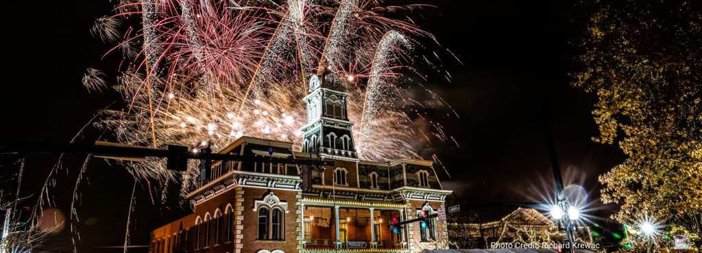 This is a photo on Realty Done by Damien Baden's webpage for Luxury Homes for Sale in Medina, Ohio. It features The historic Medina County courthouse, built in 1841, constructed in ornate Second Empire architecture with a two-story front portico and a slate mansard roof with clock tower. The building is illuminated at night by a spectacular display of colorful fireworks bursting in the dark sky above it. This festive and celebratory scene was captured during the annual holiday celebration called Candlelight Walk. Photo Credit: Richard Krewac.