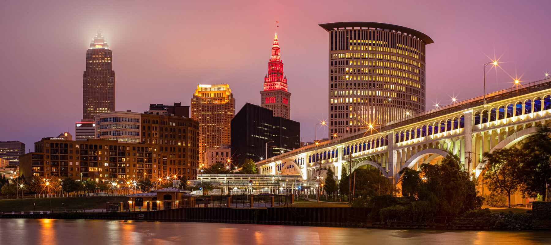 Downtown Cleveland skyline at dusk with illuminated skyscrapers and the brightly lit Veterans Memorial Bridge over The Cuyahoga River. This is the cover photo for Realty Done by Damien Baden's homepage – the best real estate agent to help you buy and sell homes in Northeast Ohio.