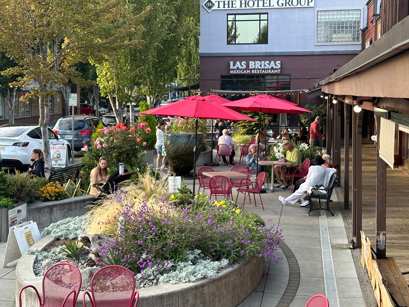 Lively outdoor scene at the Edmonds Art Walk – visitors enjoying art, food, and community under vibrant red umbrellas.