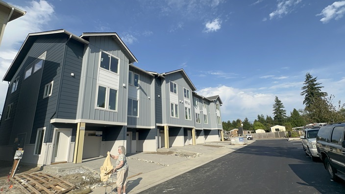 Row of new townhomes in Everett, WA, featuring gray exteriors and spacious garages, set against a clear blue sky.