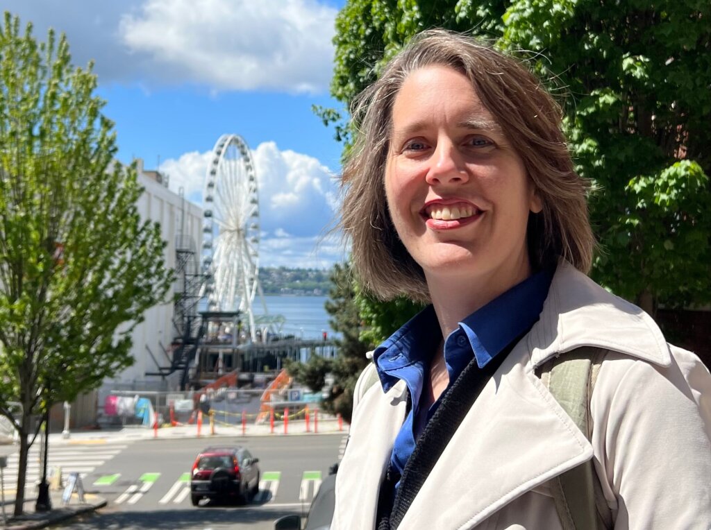 Emily Cressey strolling around the heart of Seattle, overlooking the Seattle Great Wheel, navigating the busy street in Downtown Seattle