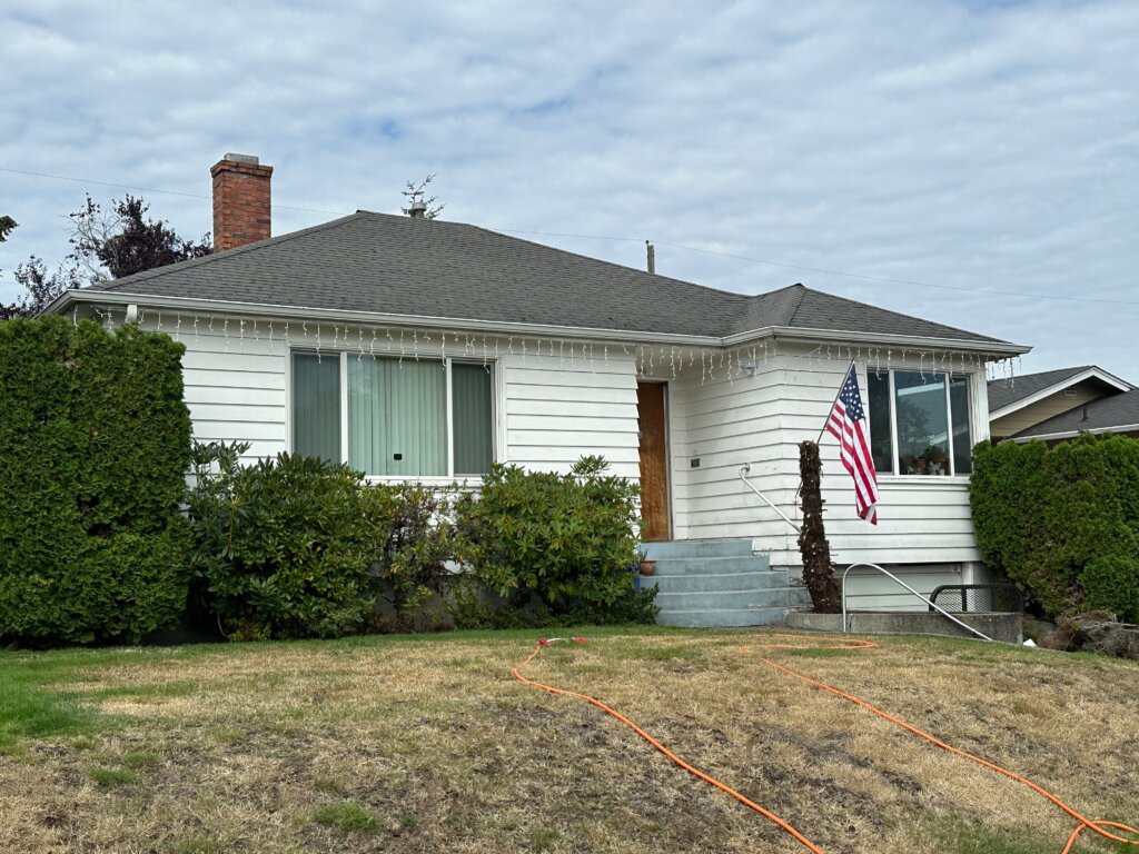 Traditional white rambler in Tacoma with well-kept lawn, large front window, and American flag displayed.
