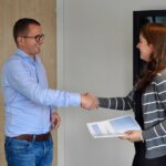 two people shaking hands with one holding a folder