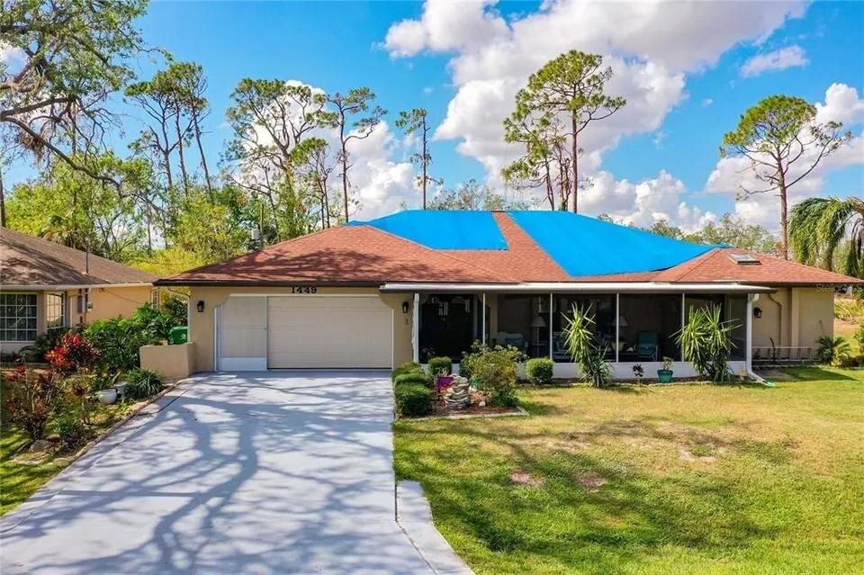 Florida single-story house with blue tarps covering a storm-damaged roof, attached garage, and front lawn.
