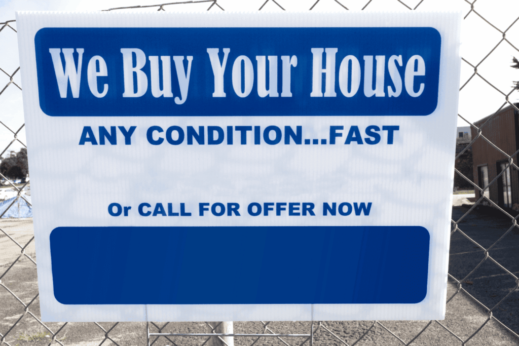 Blue and white sign reading “We Buy Your House Any Condition... Fast Call for Offer Now,” attached to a chain-link fence