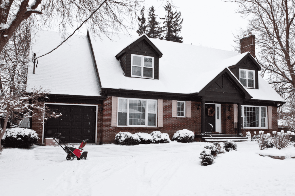 Brick house covered in snow with a snowblower on the driveway.
