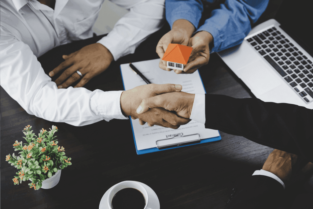 Businesspeople shaking hands over a contract with a small house model on the table