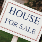Close-up of a house for sale sign posted in front of a home.