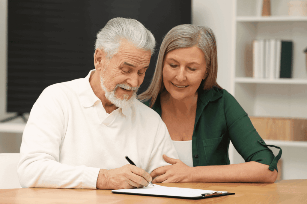 Elderly couple sitting together as the man signs a document.