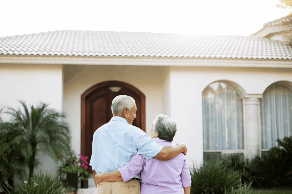 Elderly couple standing arm in arm in front of their house.