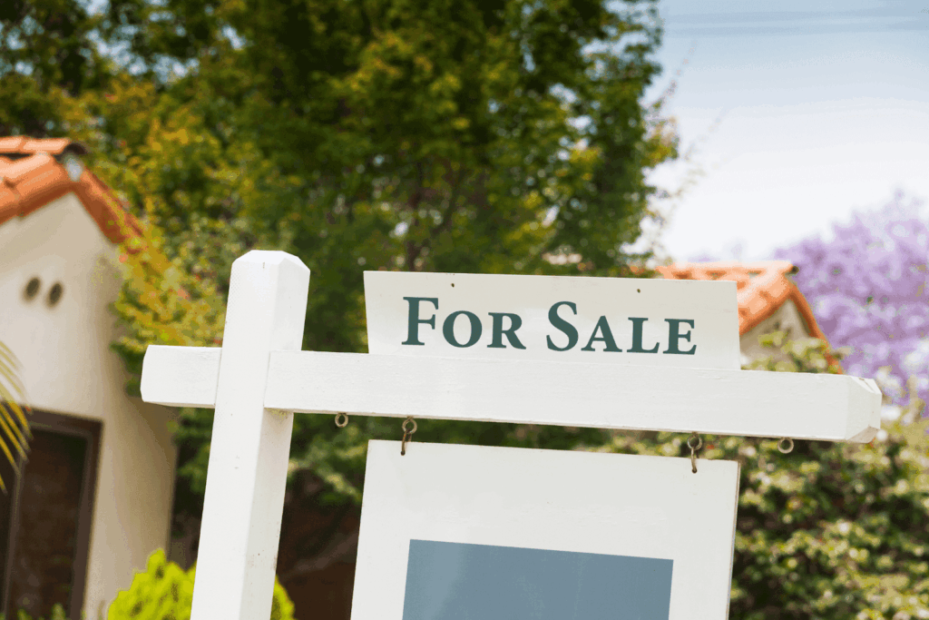 For Sale sign in front of a house with trees in the background