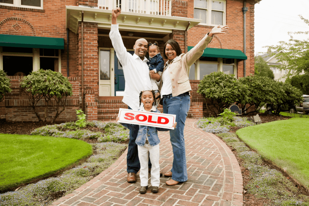 Happy family standing in front of a house holding a sold sign.