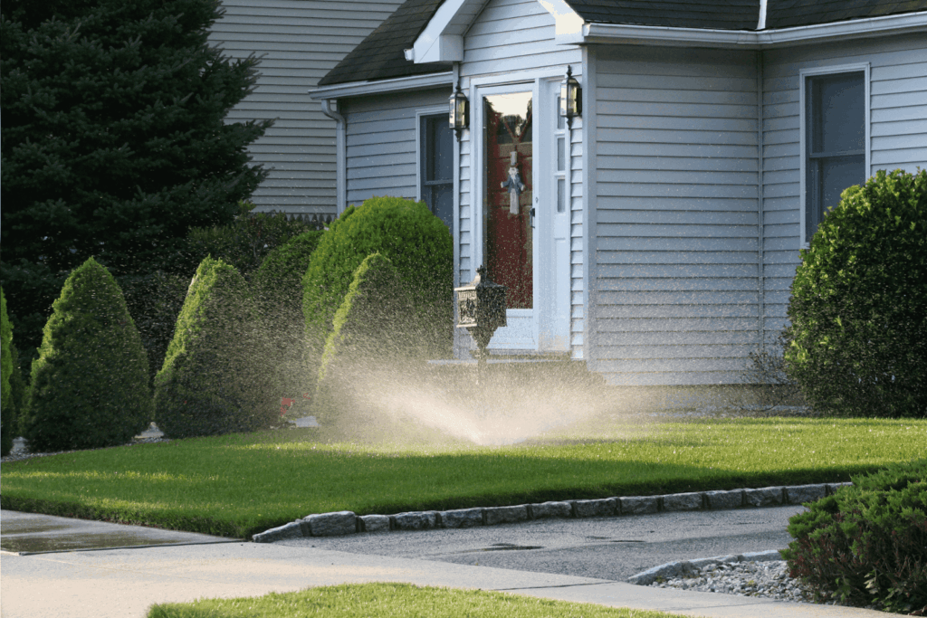 Lawn sprinkler watering grass in front of a suburban home.
