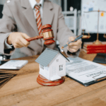 Lawyer holding a gavel near a small house model and contract documents, symbolizing property or real estate law.