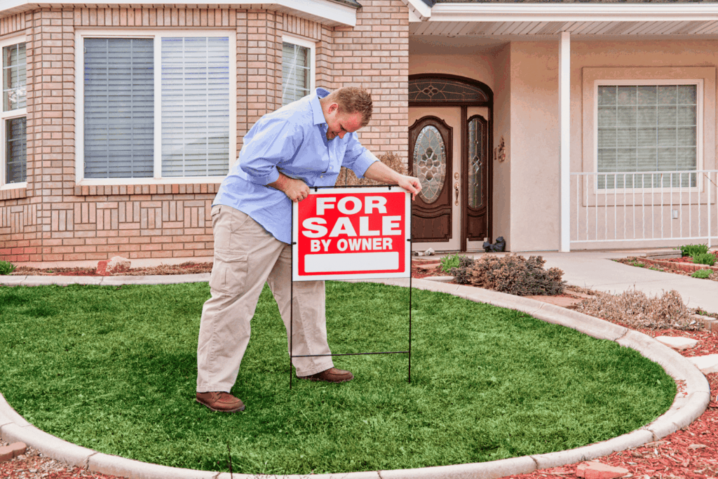 Man placing a For Sale by Owner sign in front yard of house.