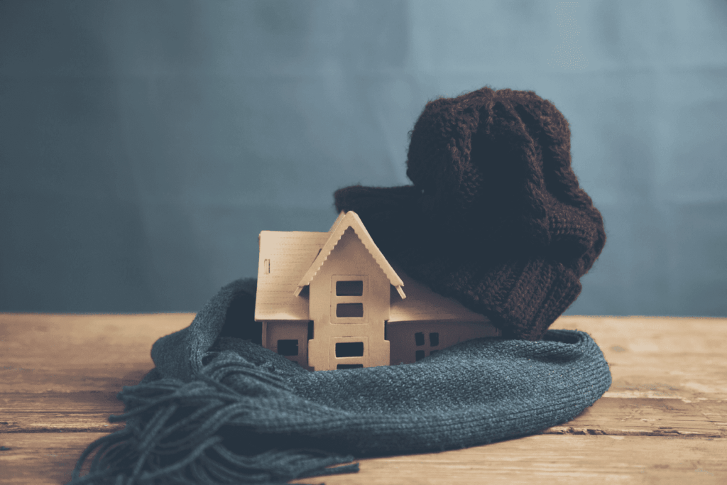 Mini wooden house wrapped in a knit hat and scarf on a table
