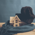 Mini wooden house wrapped in a knit hat and scarf on a table