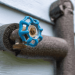 Outdoor water spigot wrapped in pipe insulation with blue valve handle.