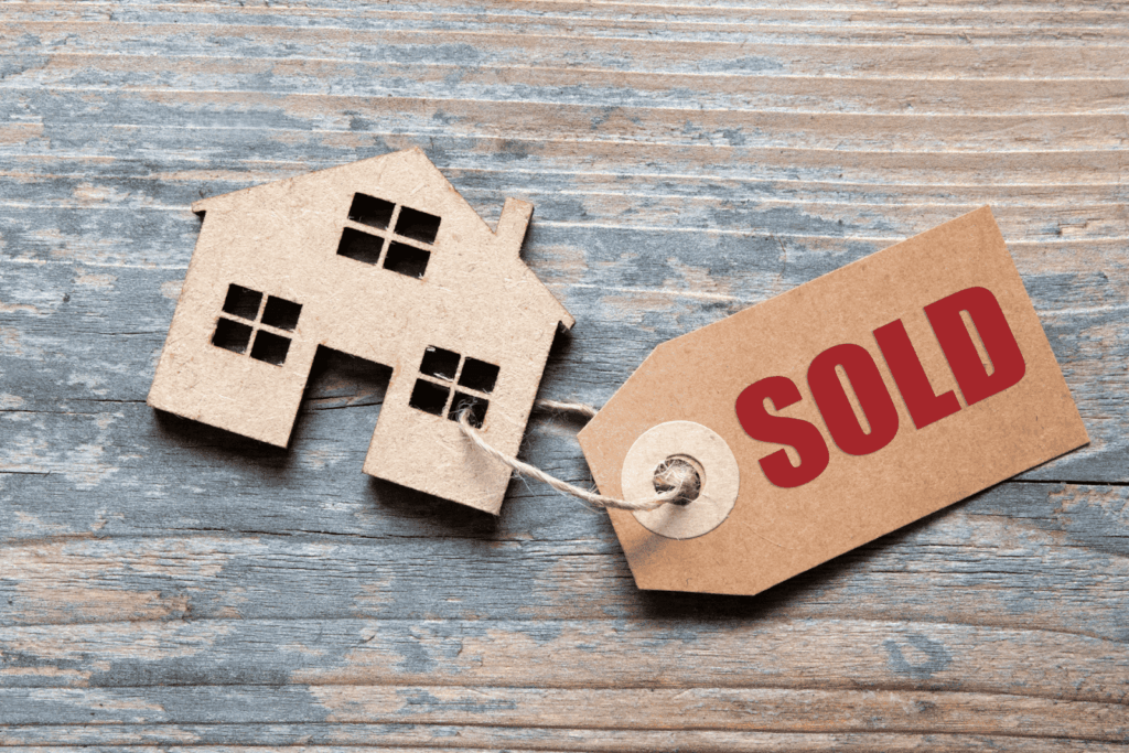 Paper house cutout with a tag labeled SOLD on a wooden surface